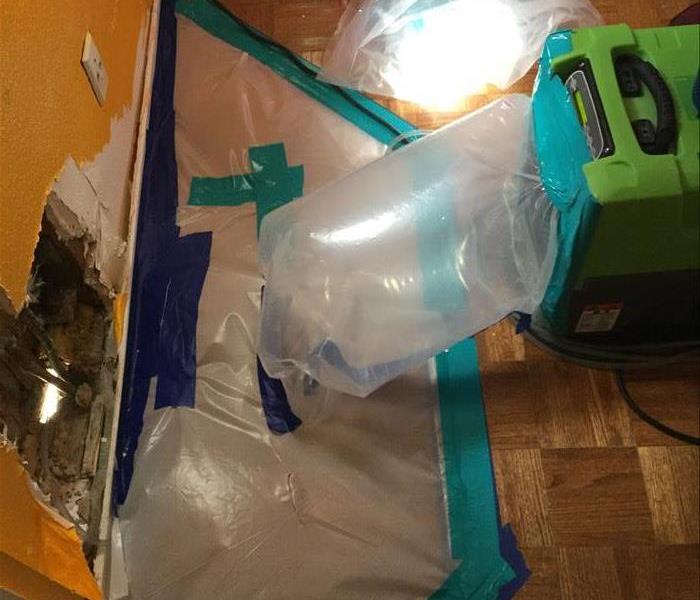 plastic containment sealed with blue tabe and a tunnel created leading to an air mover which will dry the damp area
