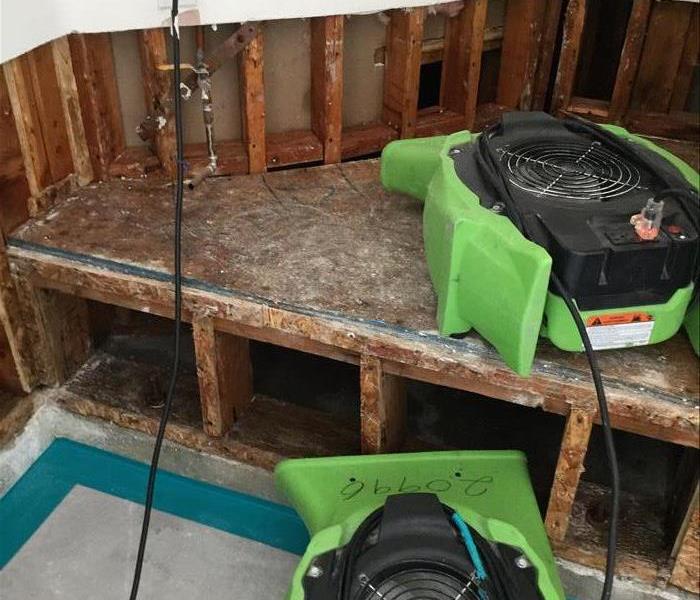 two green air movers placed facing an exposed wall and under the stair