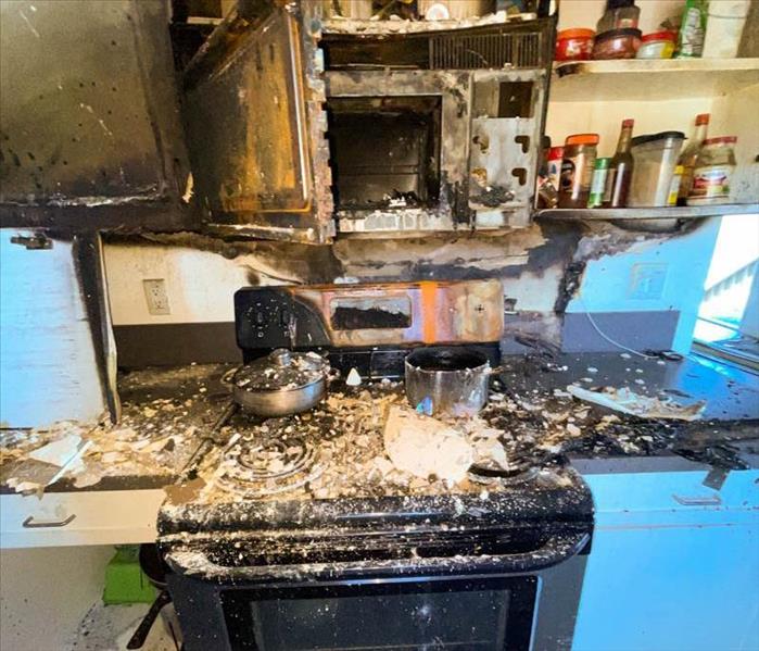 The stove and microwave area in a kitchen with severe fire damage.