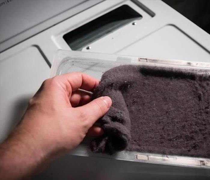 Hand cleaning accumulated clothing lint from trap in clothes dryer.